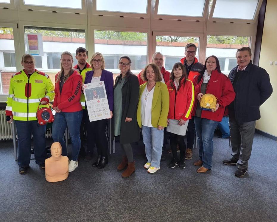 Eine Personengruppe teils in Sanitäterkleidung mit Reanimationspuppe und Defibrillatoren